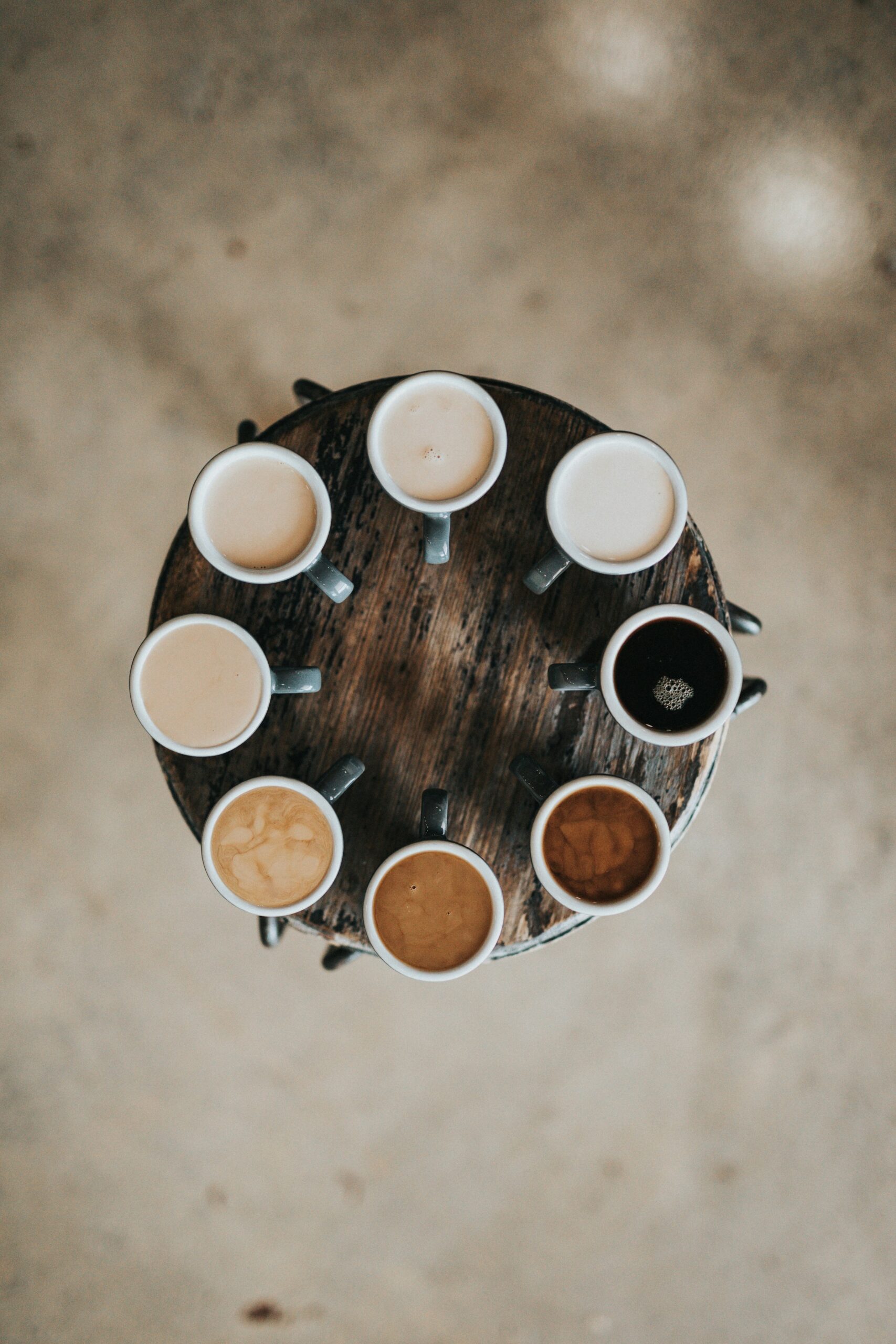 Eight cups of tea sit on a wooden table, each one is made to a different strength showing diverse preferences and attention to detail.