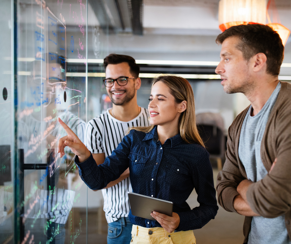 Three colleagues gather around a white board as one member points out a key bit of information